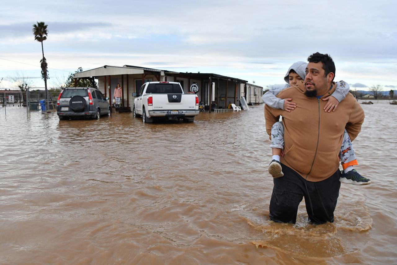 Ryan Orosco carries his 7-year-old son, Johnny, on his back while his wife, Amanda, waits at the front porch to be rescued from their flooded home in Brentwood, California, on Monday, January 16.