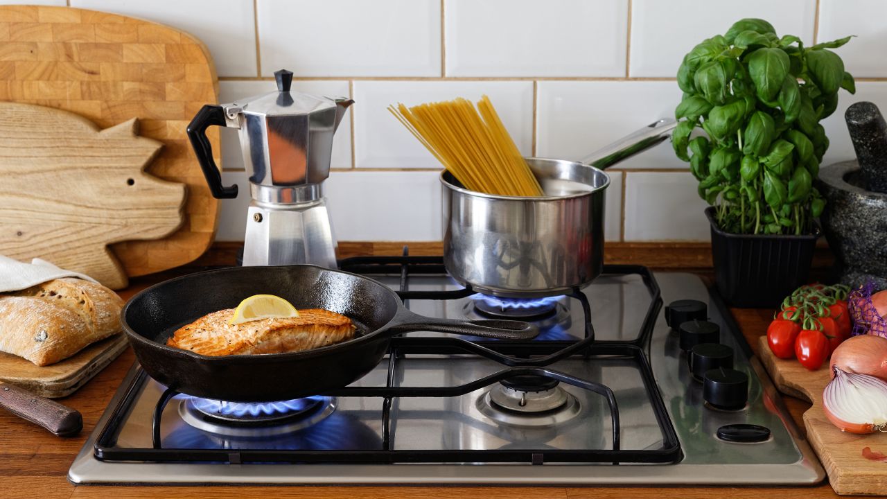 Pan fried salmon fillet and spaghetti on a gas stove in traditional home kitchen. Wood worktop.