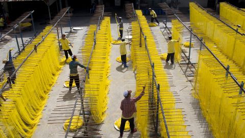 Workers remove longevity noodles from racks after they have dried in the sun at a factory in Thailand.