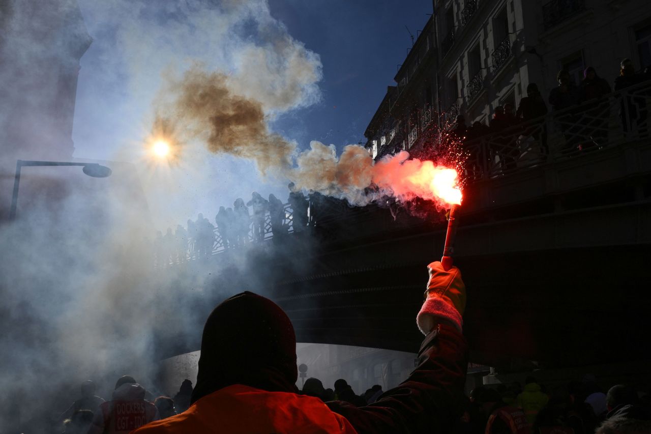 A protester waves a flare during a rally called by French trade unions against the <a href=