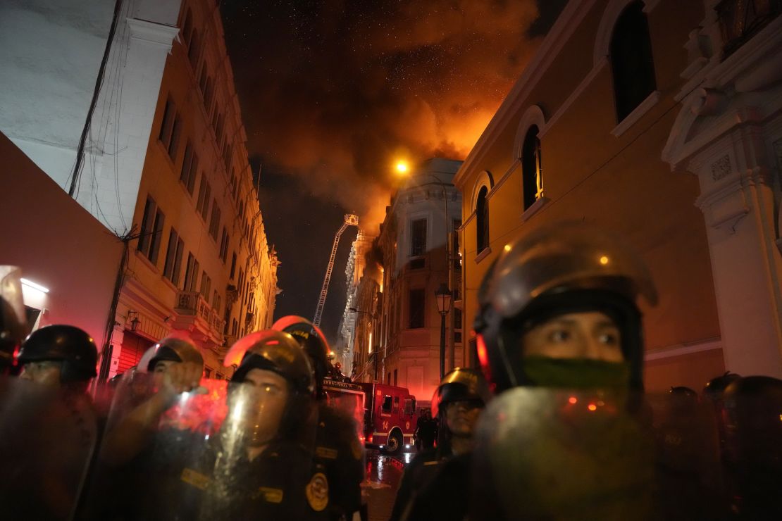 Police in riot gear block a street as a building burns behind them in Lima, Peru, Thursday.