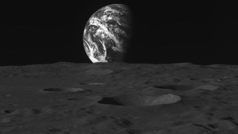 The moon's heavily cratered surface can be seen as Earth rises above it.