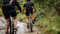 two cyclists riding mountain bike on dirty trail in forest
