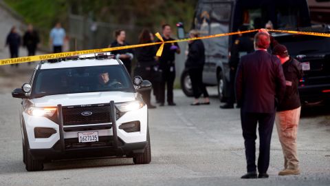 A San Mateo County deputy holds up crime scene tape as a vehicle drives past where several people were shot and killed in Half Moon Bay, California on Monday.