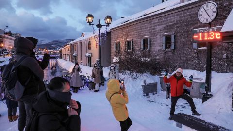 Toeristen poseren voor foto's voor een thermometer die -11,3 graden Celsius aangeeft, in Otaru, Hokkaido prefectuur in het noorden van Japan op 24 januari 2023.