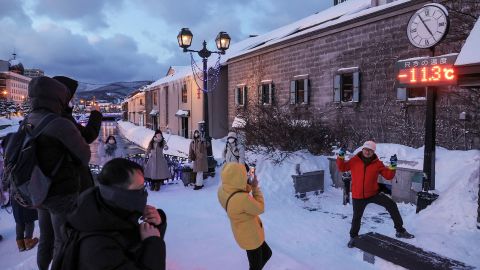 Toeristen poseren voor foto's voor een thermometer die 11,3 graden Celsius (11,6 Fahrenheit) bereikt, in Otaru, de prefectuur Hokkaido in het noorden van Japan op 24 januari 2023.