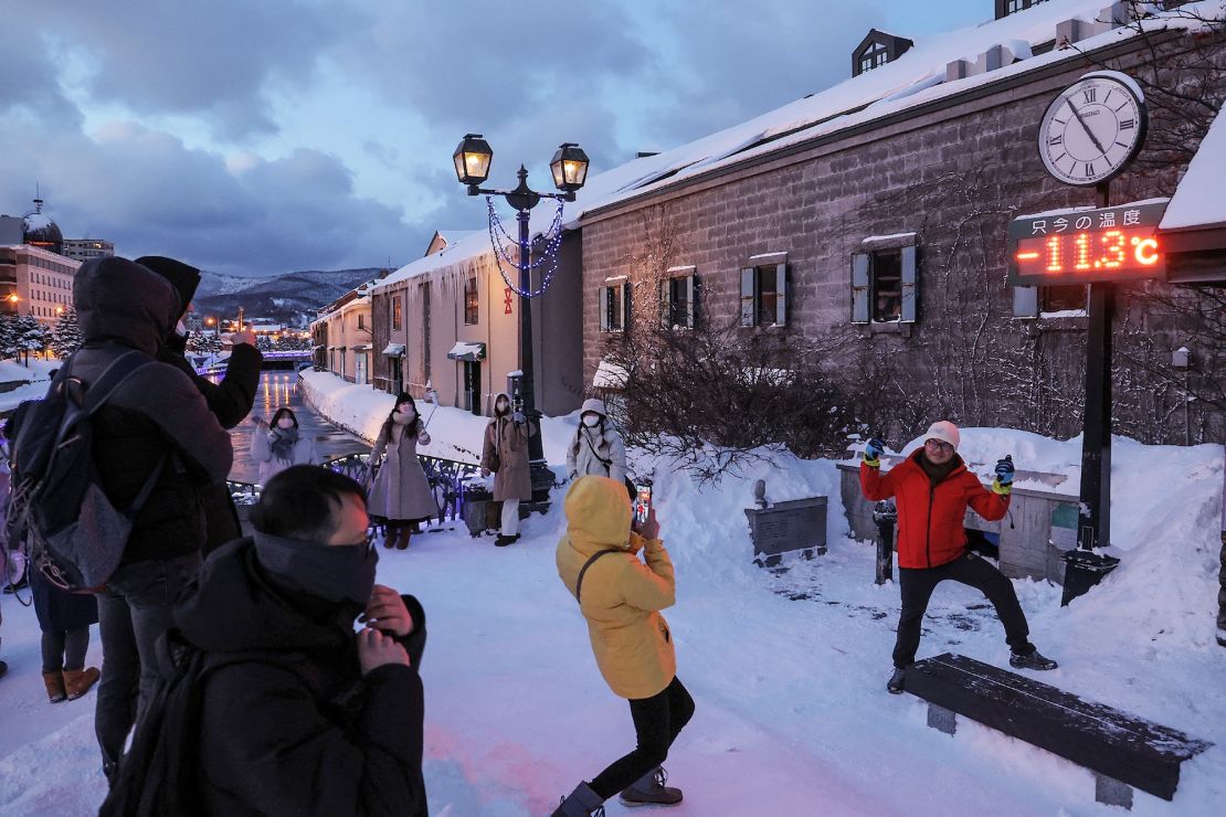 Tourists pose for photos in front of a thermometer reading -11.3 degrees Celsius (11.6 F), in Otaru, Hokkaido prefecture of northern Japan on January 24, 2023.