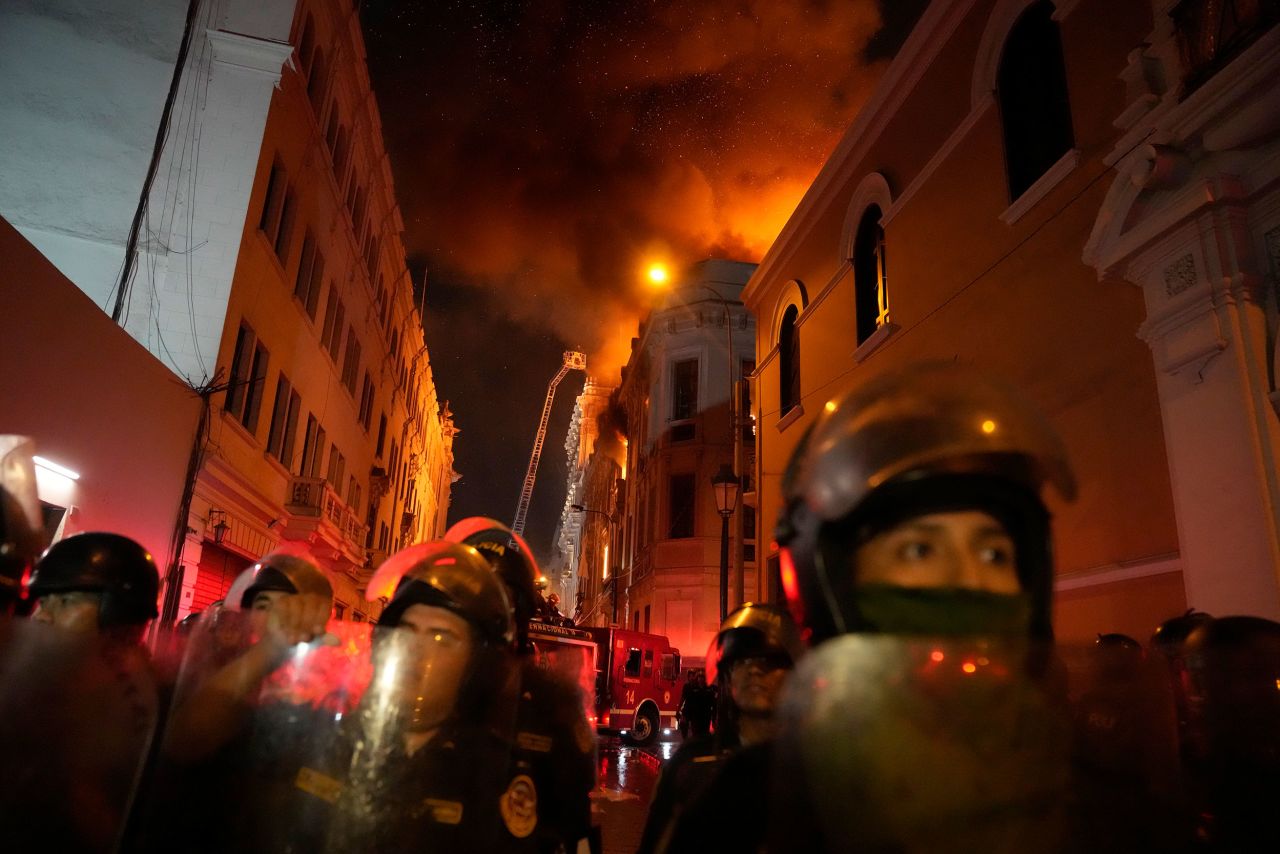 Police block a street in Lima, Peru, as a building burns behind them on Thursday, January 19. Peruvian President Dina Boluarte called for dialogue after clashes between protesters and police during nationwide demonstrations. <a href=