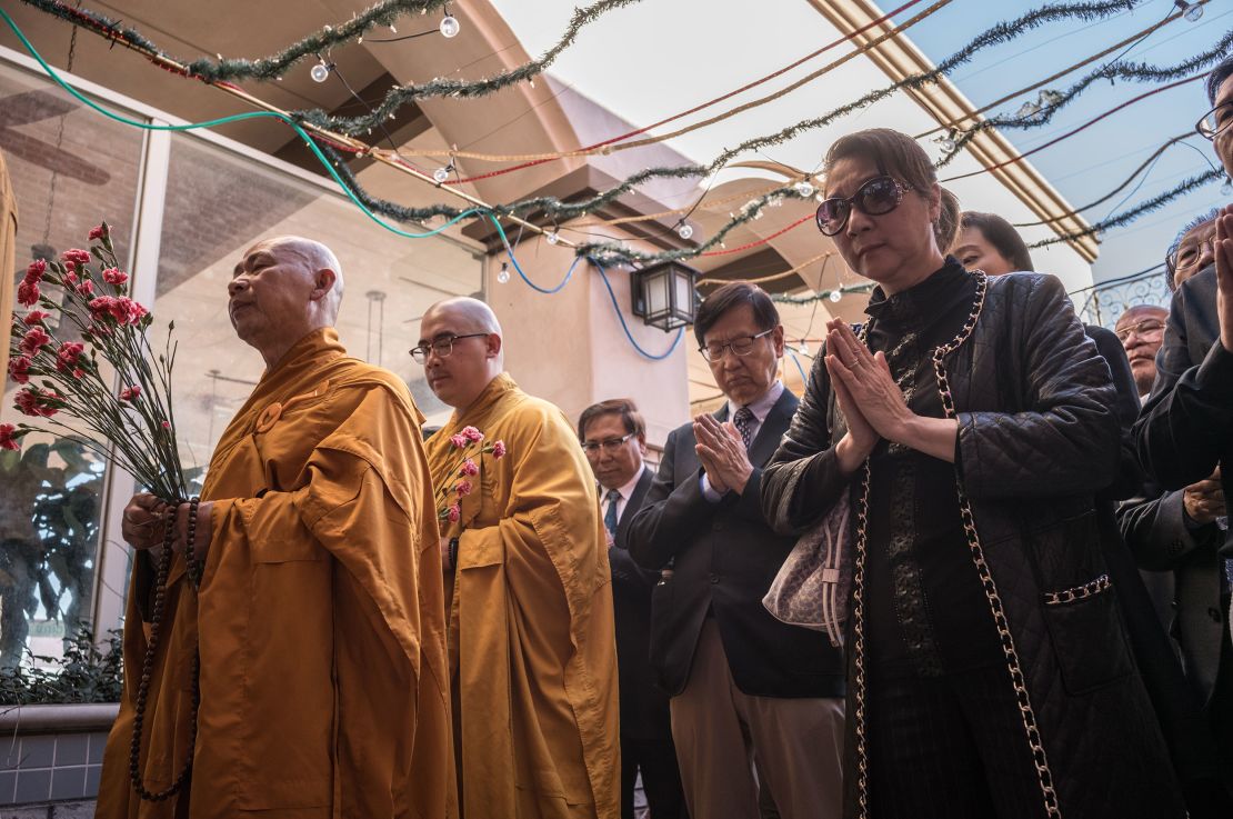 Maria Liang, right, prays at the entrance of the dance studio during a ceremony led by Buddhist monks honoring the victims. 