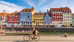 Copenhagen, Denmark - July, 2019: Copenhagen iconic view. Famous old Nyhavn port with colorful medieval houses, tourist ship and woman on a bicycle in the center of Copenhagen. Selective focus.
