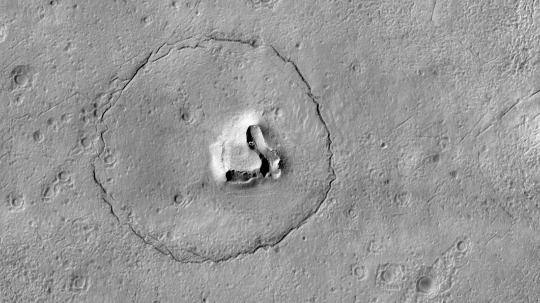 The face of a bear appears to take shape on the Martian surface in this new image taken by the HiRISE camera aboard the Mars Reconnaissance Orbiter. Two craters create the eyes, a circular fracture shapes the face, and a V-shaped collapse structure represents the nose. 