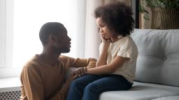 Loving african American father talk with upset preschooler daughter helping with problem, caring black young dad speak with sad girl child holding caressing hand, show support and understanding.