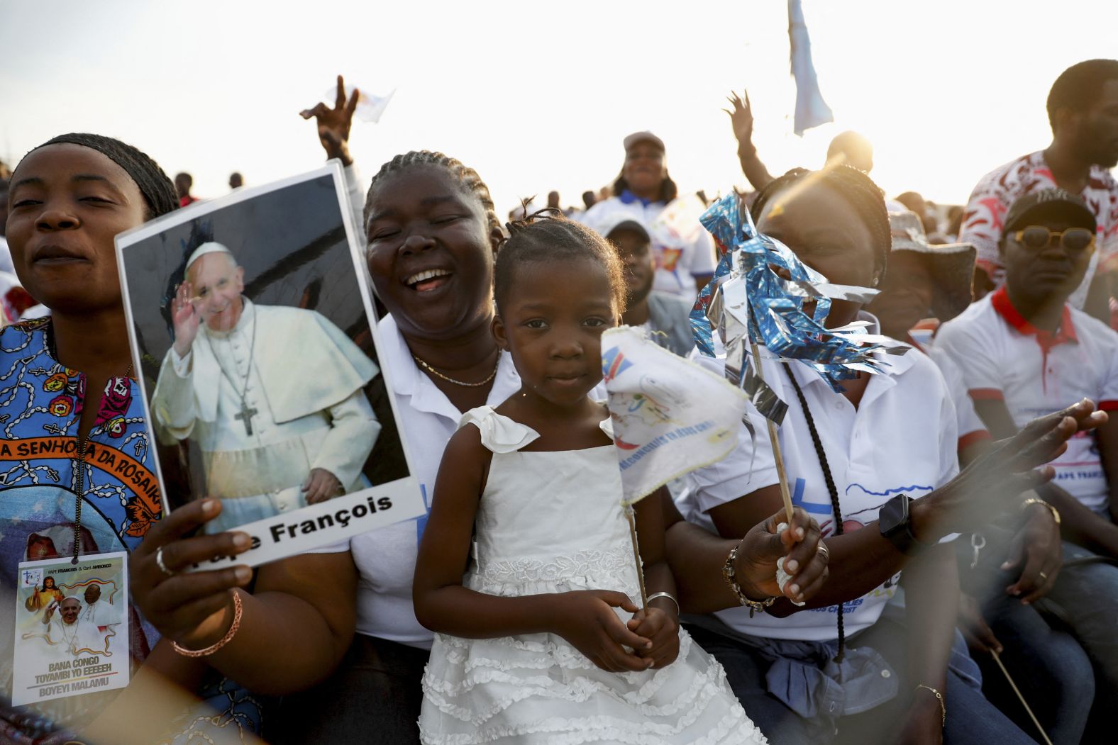 A woman with a child holds an image of Pope Francis at N'Dolo Airport.