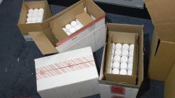 Three open cardboard boxes filled with white pill bottles and one sealed with security tape