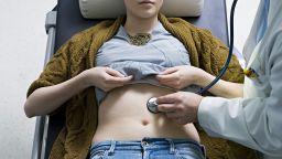 Doctor examing woman`s stomach with stethoscope - stock photo