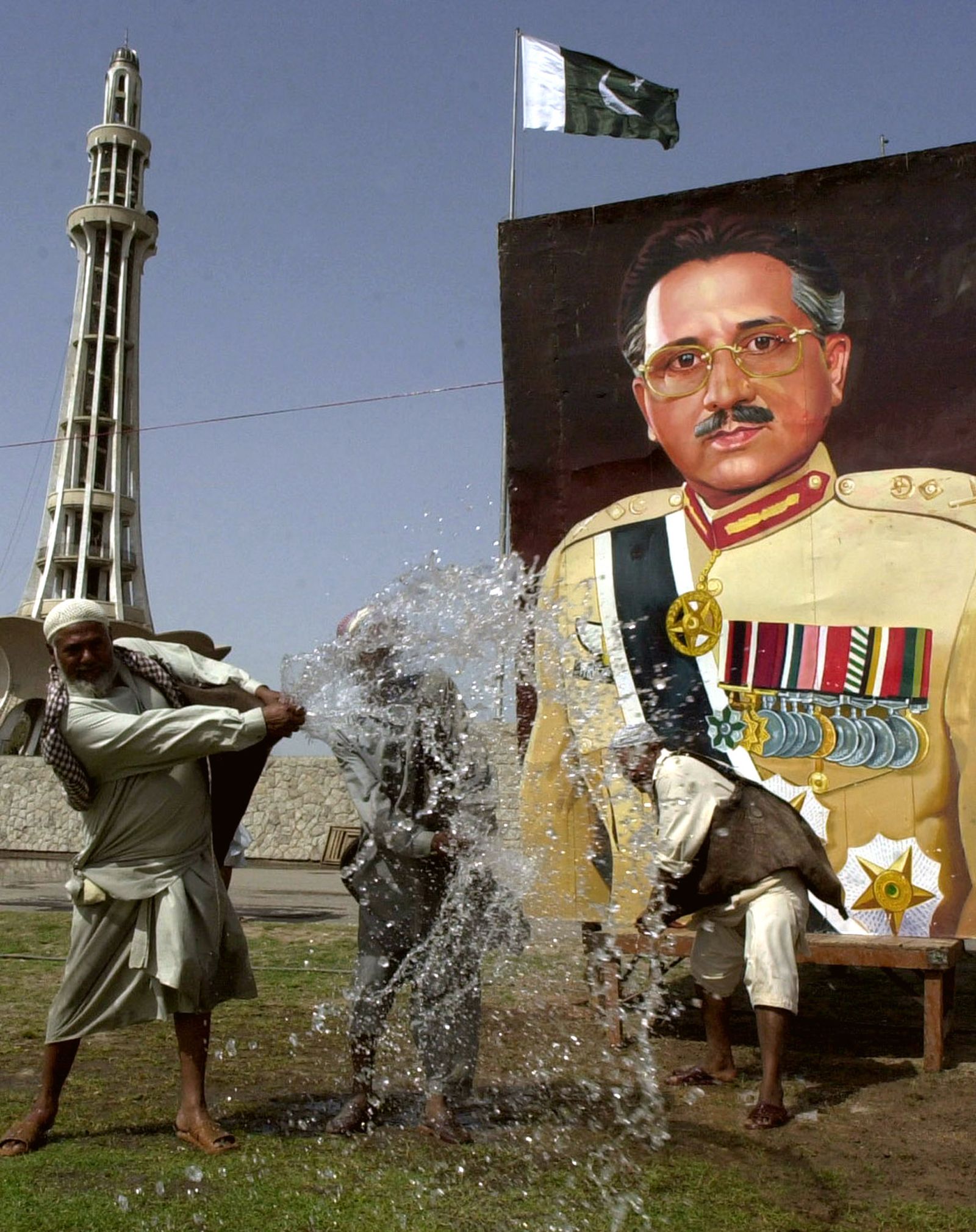 Workers sprinkle water on lawn in Lahore, near a portrait of Musharraf, in April 2002.