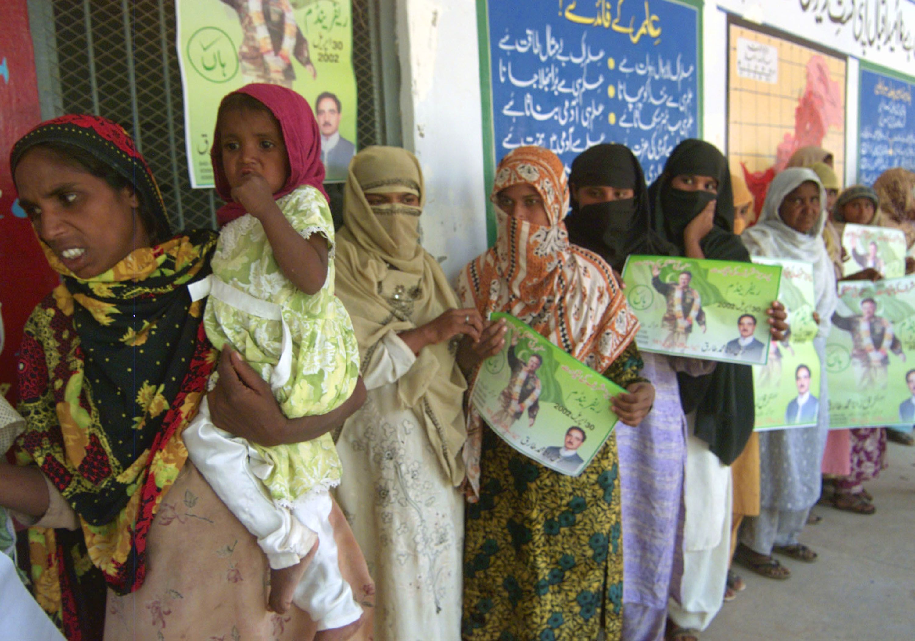 Pakistani women hold pictures of Musharraf as they stand outside a polling station in Lahore during the 2002 referendum.