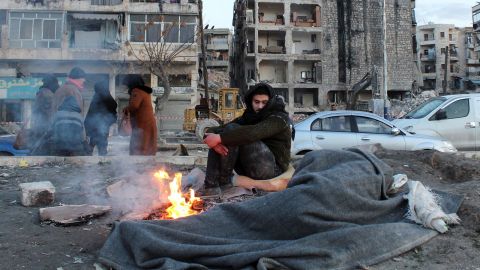A man who evacuated his home warms up next to a fire in the aftermath of the earthquake, in Aleppo, Syria, February 8, 2023.