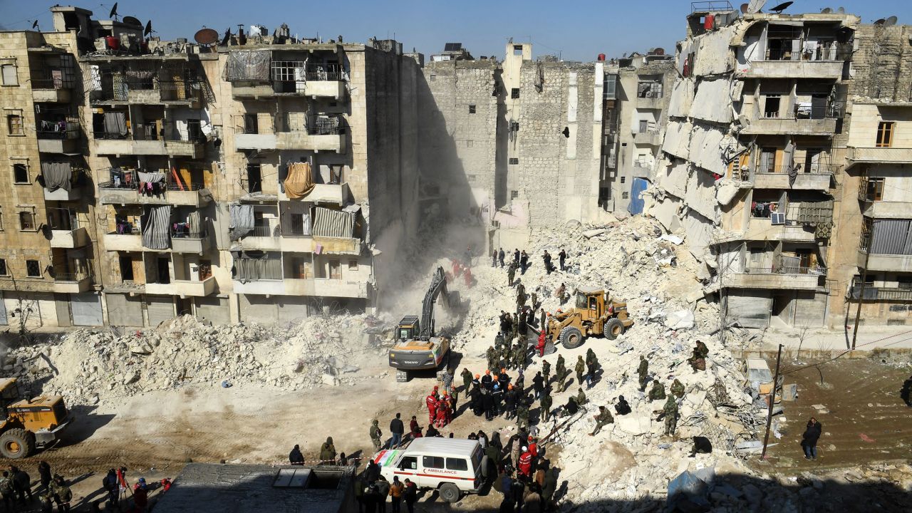  Syrian soldiers look on as rescuers use heavy machinery sift through the rubble of a collapsed building in the northern city of Aleppo on February 9, 2023. 