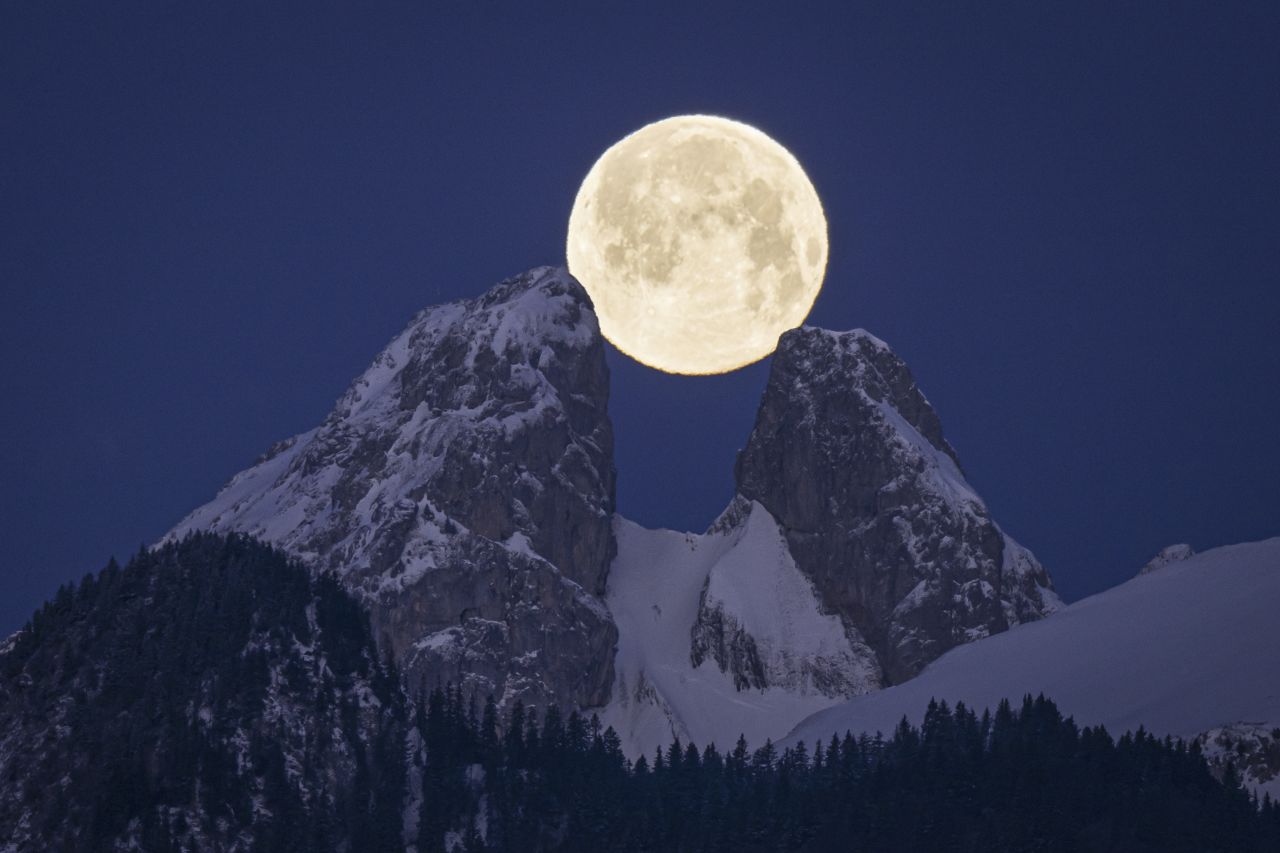 The full moon sets behind mountains, including the twin peaks of Les Jumelles, near Aigle, Switzerland, on Monday, February 6.