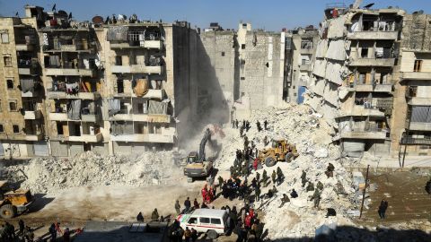 Syrian soldiers look on as rescuers use heavy machinery to sift through the rubble of a collapsed building in the northern city of Aleppo.