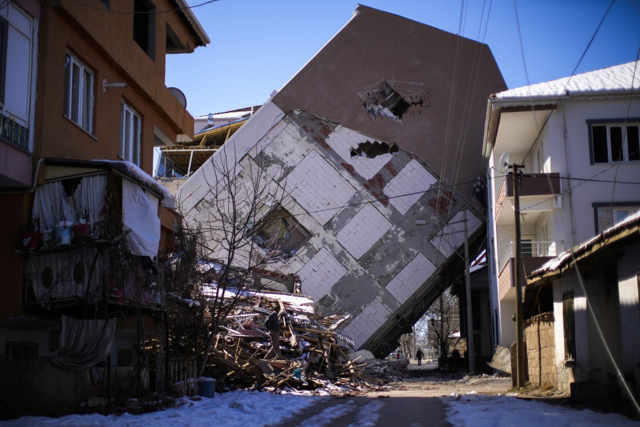 A man walks near a building that toppled over onto a neighboring structure in Golbasi, Turkey, on Monday, February 13.
