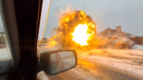 Dos imágenes tomadas de imágenes de teléfonos móviles muestran los momentos antes y después de que la ambulancia fuera alcanzada por un misil.  La primera imagen muestra el misil pasando como un rayo por un vehículo incendiado;  el segundo muestra su impacto.