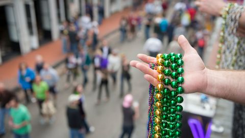A man holds several strands of Mardi Gras beads while standing on a balcony above Bourbon Street.