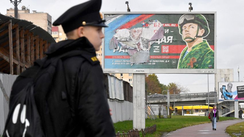 A military cadet stands in front of a billboard promoting contract army service in Saint Petersburg on October 5, 2022. - Russian President Vladimir Putin announced on September 21 a mobilisation of hundreds of thousands of Russian men to bolster Moscow's army in Ukraine, sparking demonstrations and an exodus of men abroad.