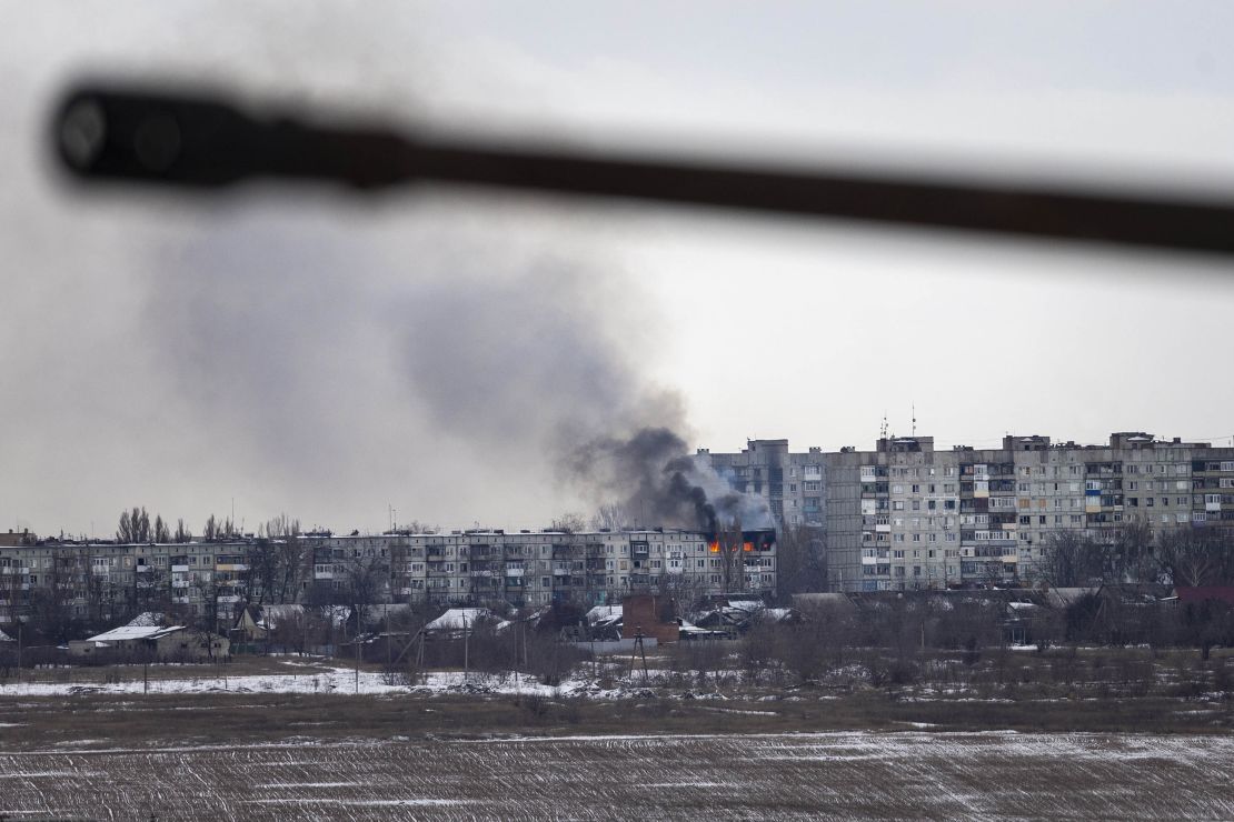 A Ukrainian military vehicle drives by as an apartment building hit by Russian artillery burns in the distance on February 14, 2023 in Bakhmut, Ukraine.