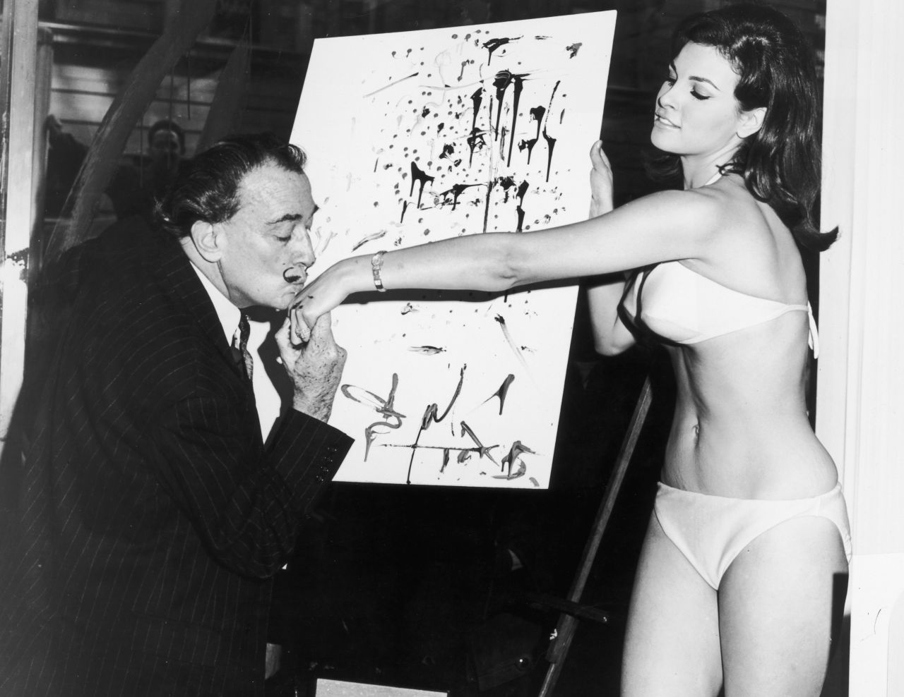 Artist Salvador Dali kisses Welch's hand in front of an abstract portrait of her circa 1965.