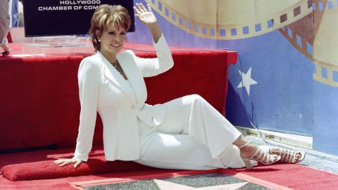Raquel Welch waves as she sits in front of her star on the Hollywood Walk of Fame in 1996 in Hollywood.