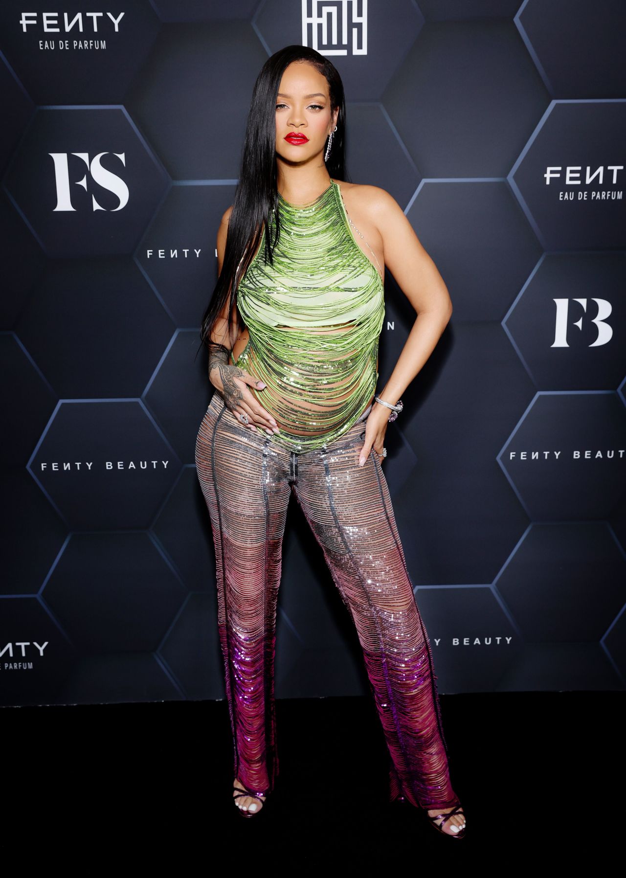 That same month, Rihanna turned heads at a Fenty Beauty Universe Event in a metallic fringe set by The Atitco. She accessorized the curve hugging green halter top and silver purple pants with chopard earrings and gold body jewelry.