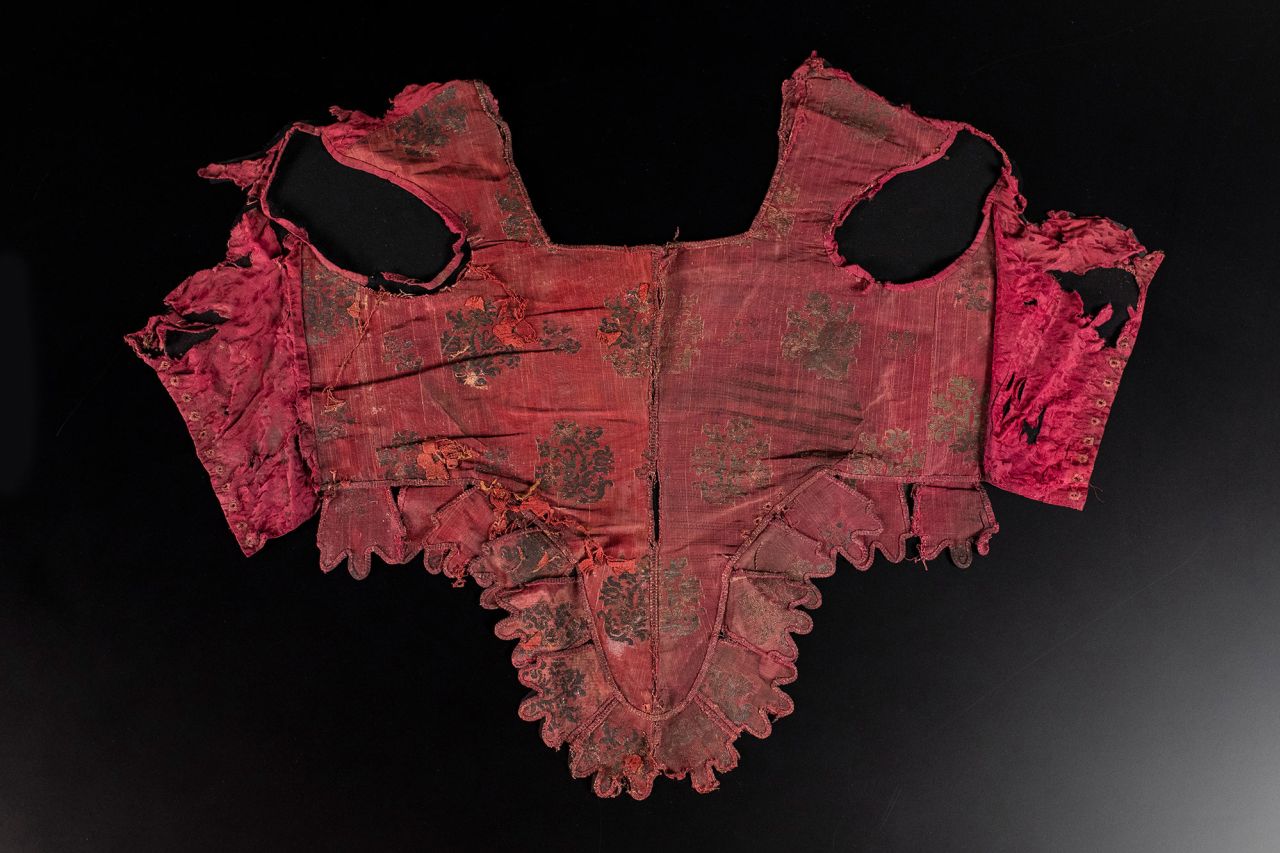 A dark red brocade bodice was also recovered from the garment chest, and impressions from the whalebone used to shape it can still be seen.