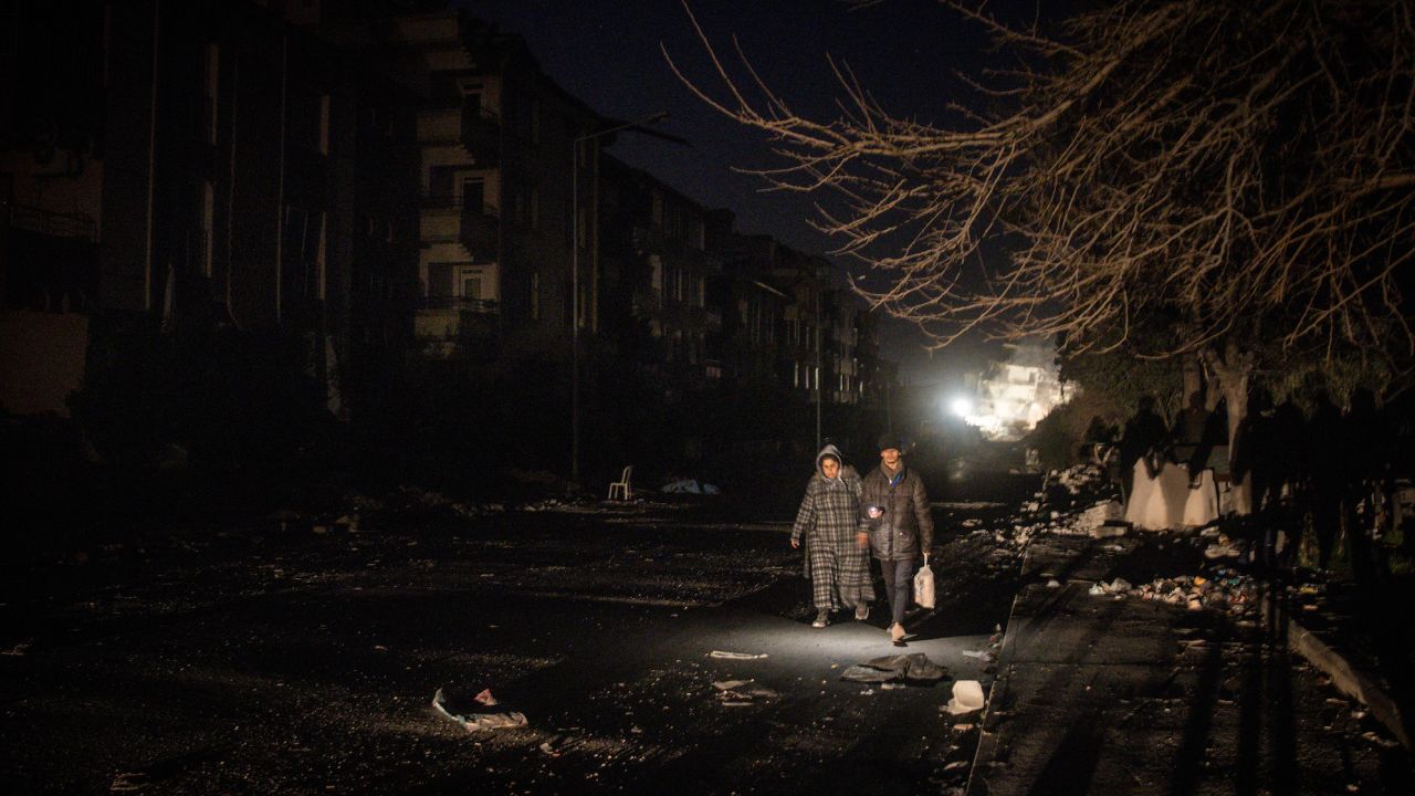 A man and woman walk along a damaged street at night in earthquake- stricken Hatay, Turkey on Thursday. 