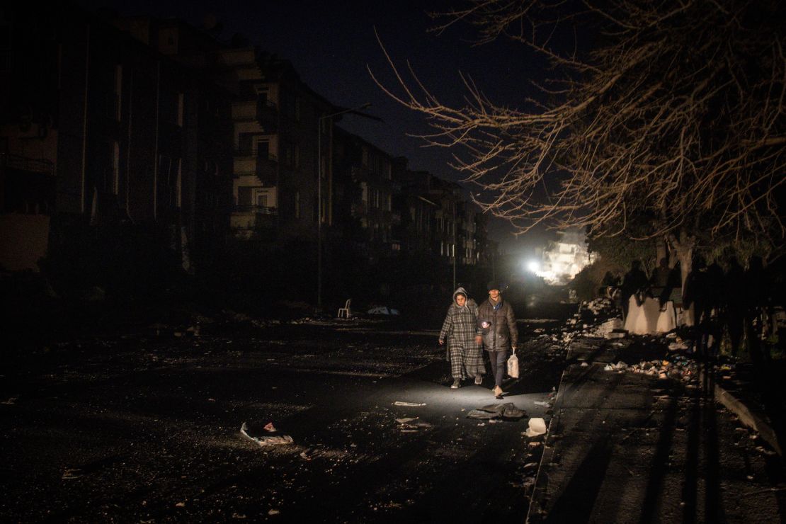 A man and woman walk along a damaged street at night in earthquake- stricken Hatay, Turkey on Thursday. 