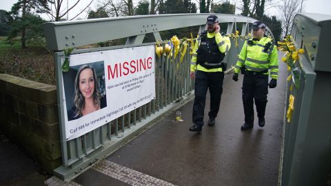 Police walk past a missing person appeal poster for Nicola Bulley.