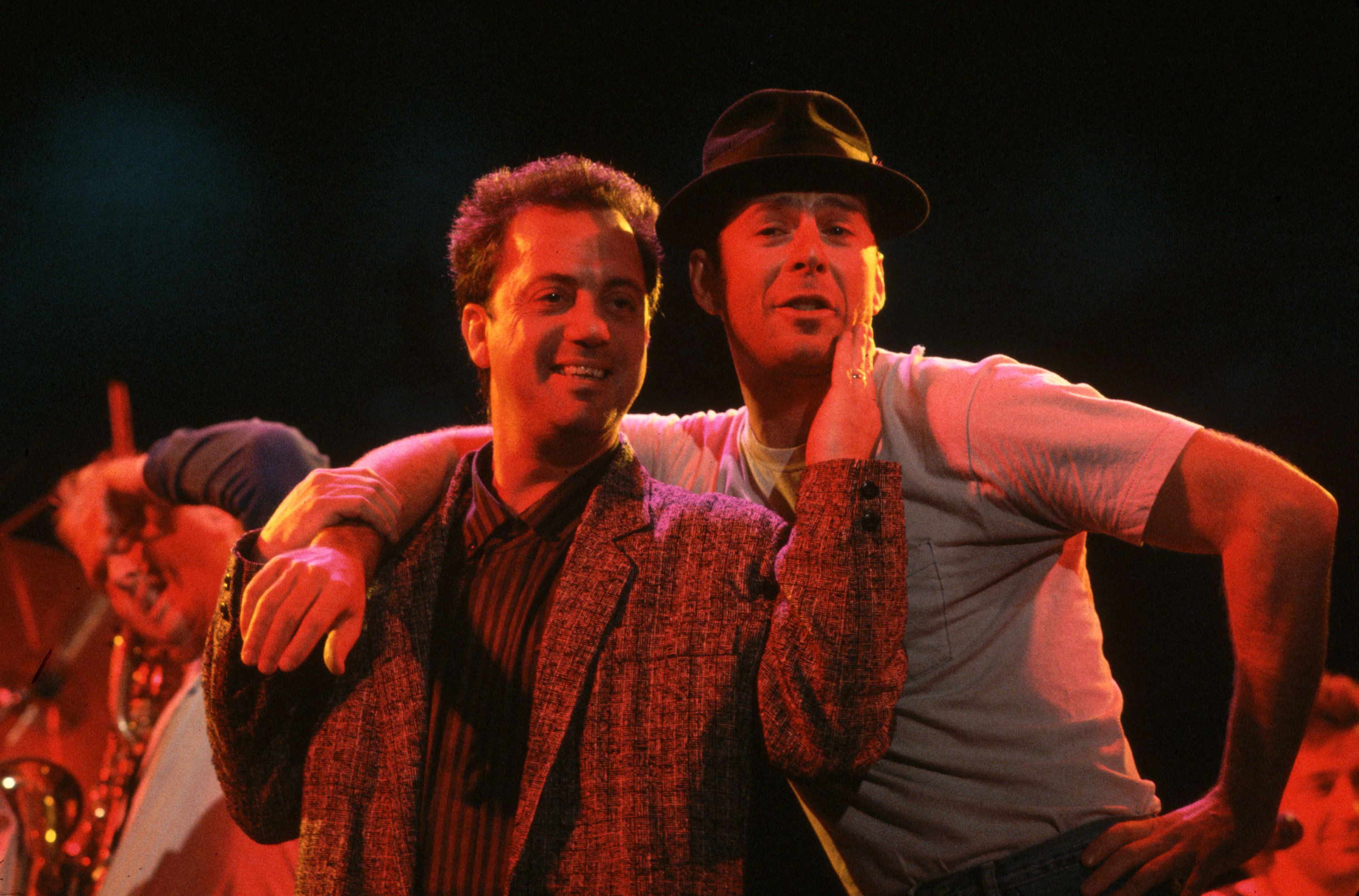 Willis puts his arm around musician Billy Joel as they sing together in New York in 1987.