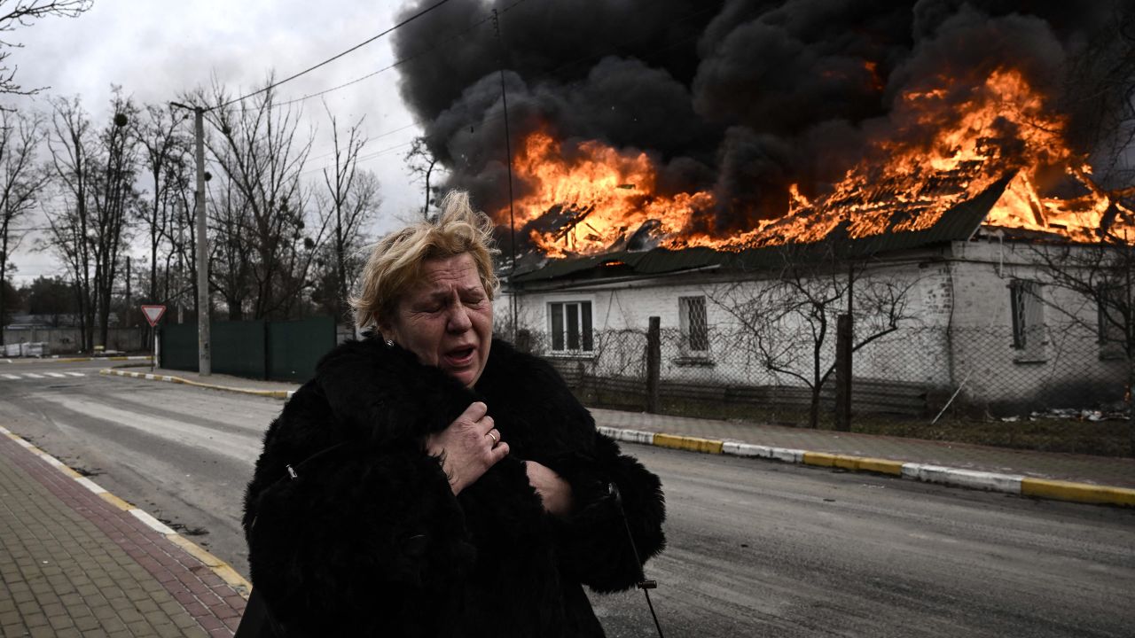 A woman stands in front of a burning house in the Ukrainian city of Irpin on March 4, 2022, days after Russia launched its invasion. 