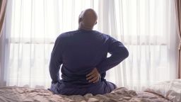 Old elderly black man. African American person waking up on bed in bedroom at home in early morning, suffering from backache or cramp. Back pain. Hurt muscle. Office syndrome.