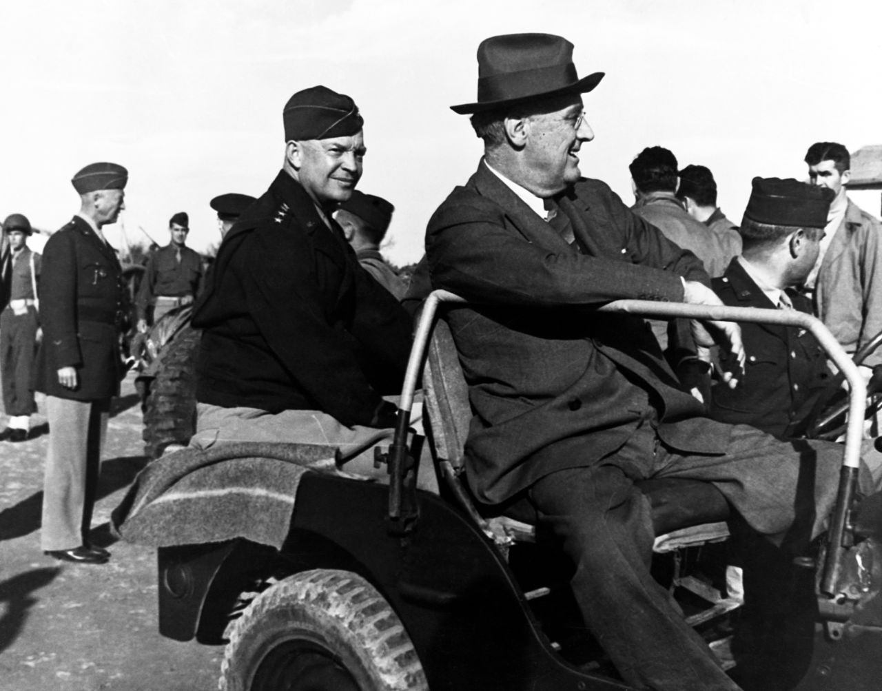 President Franklin D. Roosevelt and US Gen. Dwight D. Eisenhower share a Jeep while visiting Castelvetrano, Italy, during World War II in December 1943. Gen. George S. Patton is standing on the left.