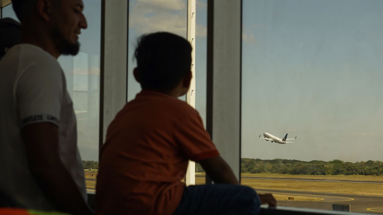 A man and his son watch a United Airlines plane take off from El Salvador International Airport.