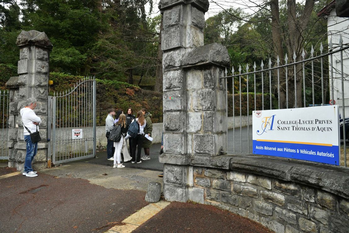 People stand at the entrance of the Saint-Thomas d'Aquin school in Saint-Jean-de-Luz, France, where a teacher died after being stabbed by a student, on February 22, 2023.