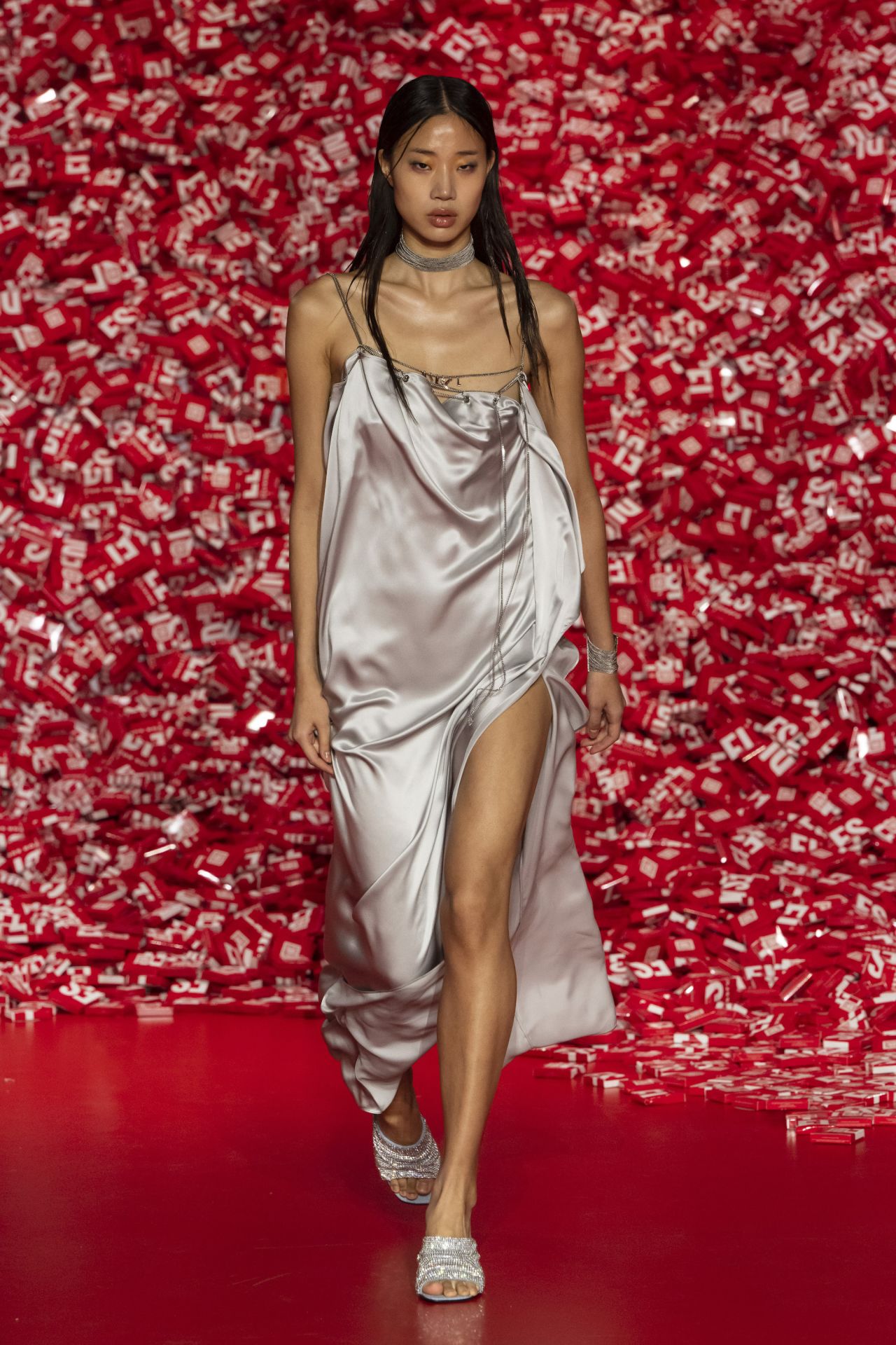 A model wearing a silk dress with draped chains on the runway.