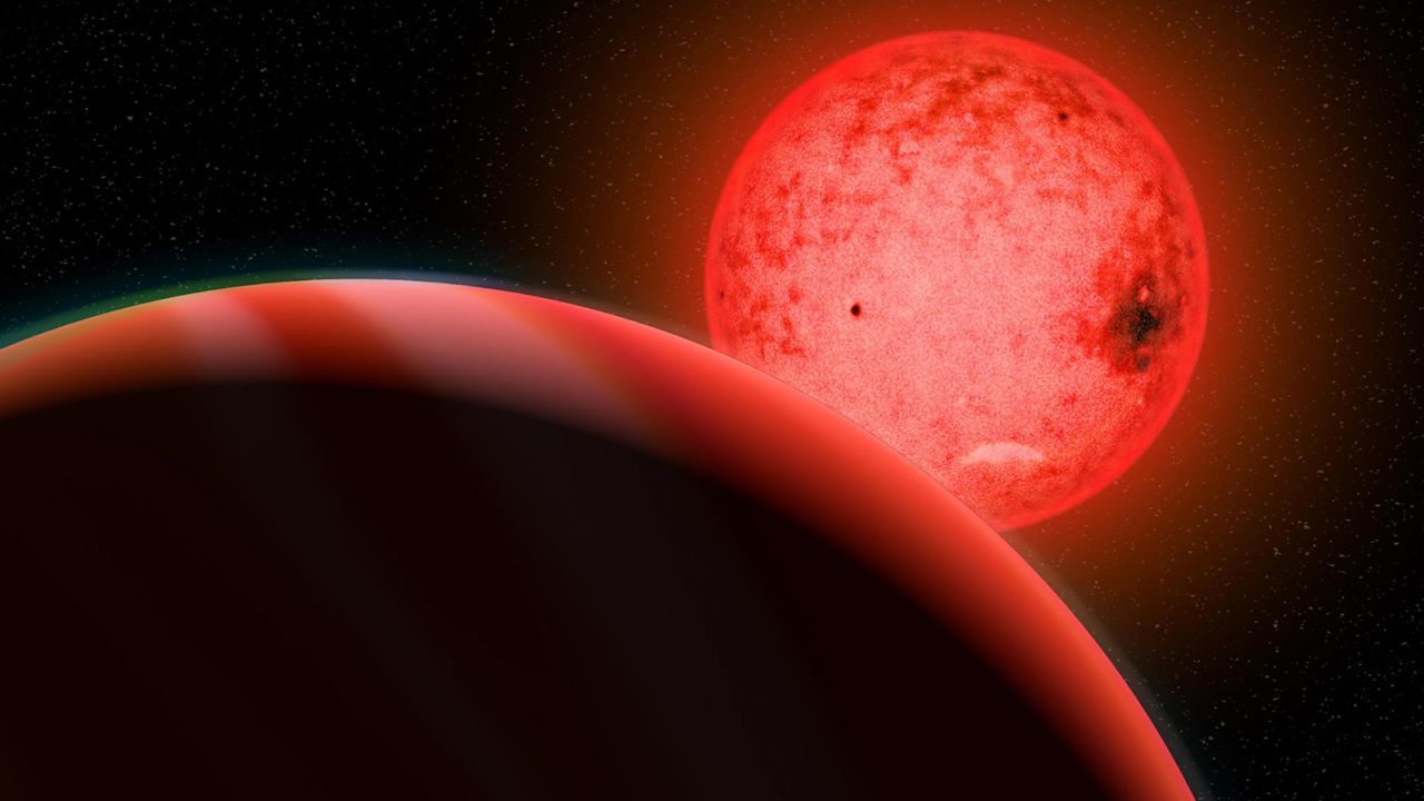 An artist's illustration shows a large gas giant planet (foreground) orbiting a small red dwarf star called TOI 5205. 