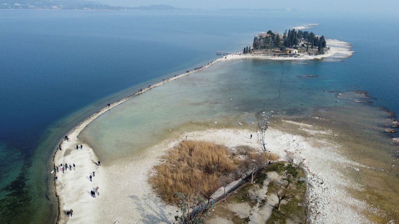 İnsanlar, 21 Şubat'ta kuzey İtalya'daki Garda Gölü'nde daha önce sular altında kalmış bir kara şeridi boyunca San Biagio Adası'na yürüyor.