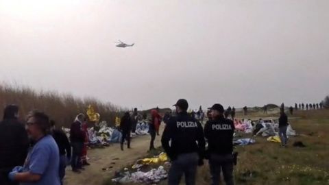 Petugas polisi berdiri di pantai tempat mayat ditemukan.  Seorang penyintas telah ditangkap atas tuduhan perdagangan migran.