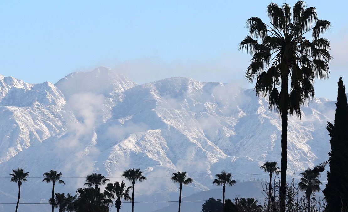 Palm trees stand in front of the snow-covered San Gabriel Mountains .