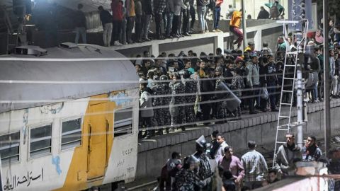 Policemen form a perimeter as people gather at the scene of a train accident in the city of Qalyub.