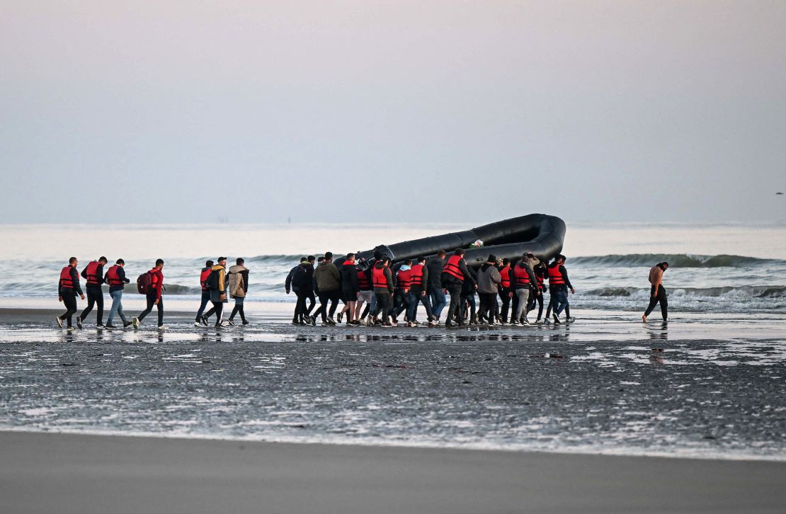 About 40 migrants, pictured on July 11, 2022, carry an inflatable boat toward the water before they attempt to cross the English Channel from northern France to reach Britain. 